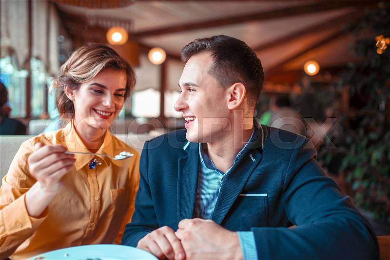Young woman feeding man with a spoon in restaurant. Love cople at romantic dinner, stock photo