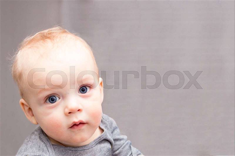Blue-eyed baby boy looking at camera with reproach. Open-eyed cute infant kid. Copy space, stock photo