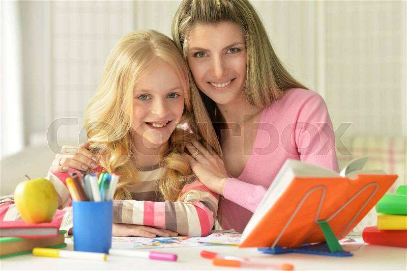 Mom and daughter doing lessons at the table, stock photo