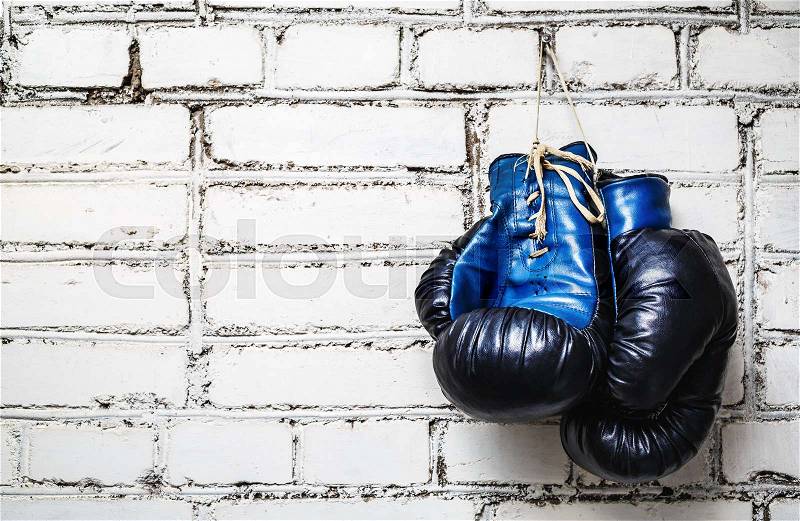 Pair of old blue and black boxing gloves hanging on white brick wall, stock photo
