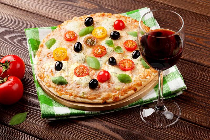 Italian pizza with cheese, tomatoes, olives, basil and red wine on wooden table, stock photo