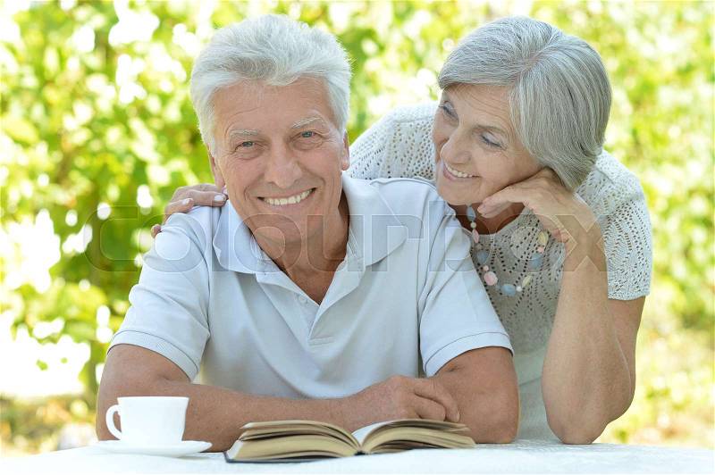 Mature couple at a table with a book in the summer, stock photo
