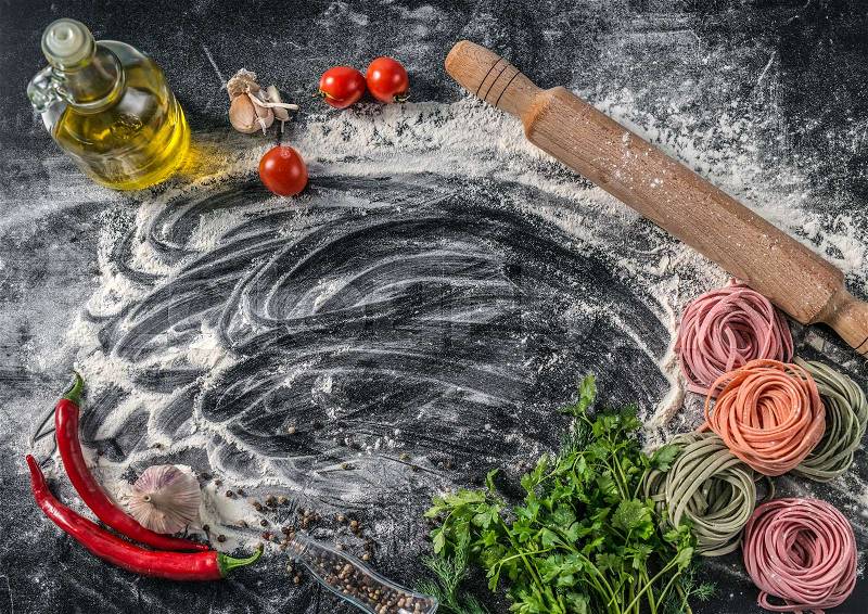 Rustic looking bottle of oil, pepper and herbs, pasta and scattered flour, copyspace in center, stock photo