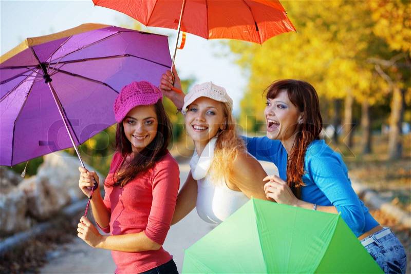 Three fashion teenage girls posing with colorful umbrellas in autumn park, stock photo