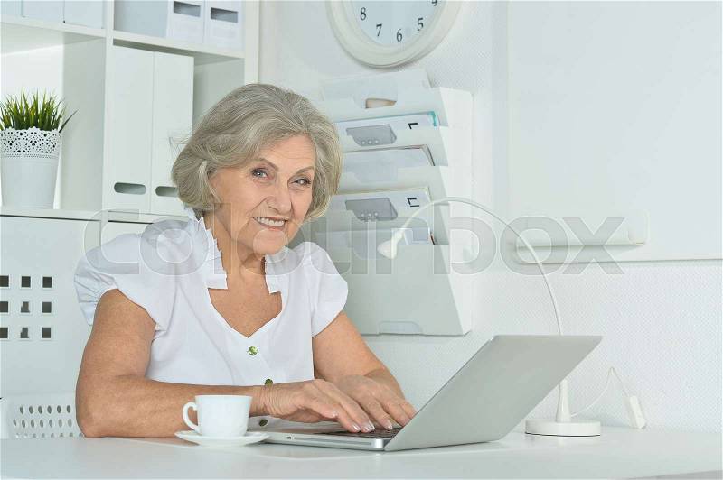 Old business woman with laptop working in the office, stock photo
