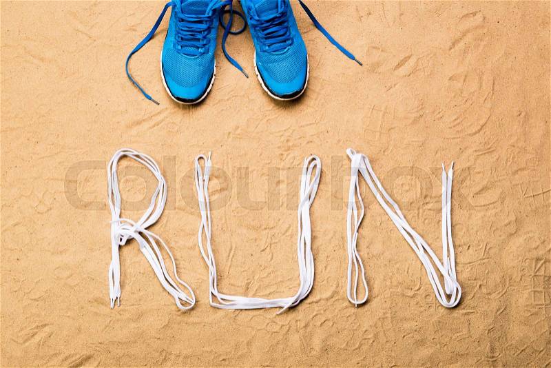 Blue running shoes and run sign made of shoelaces against sand background, studio shot, flat lay, stock photo