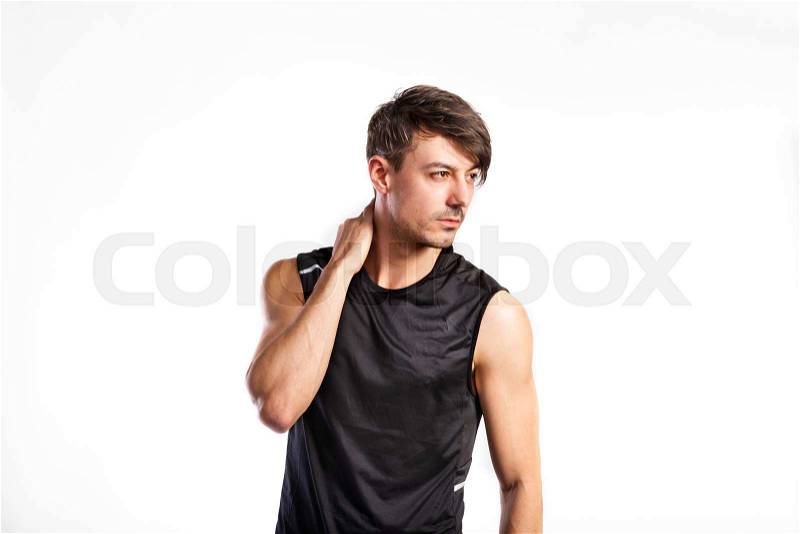 Handsome hipster fitness man in black tank top shirt, holding neck. Studio shot on gray background, stock photo