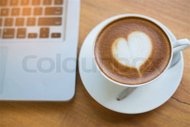 A cup of coffee with heart pattern in a white cup on wooden background, stock photo