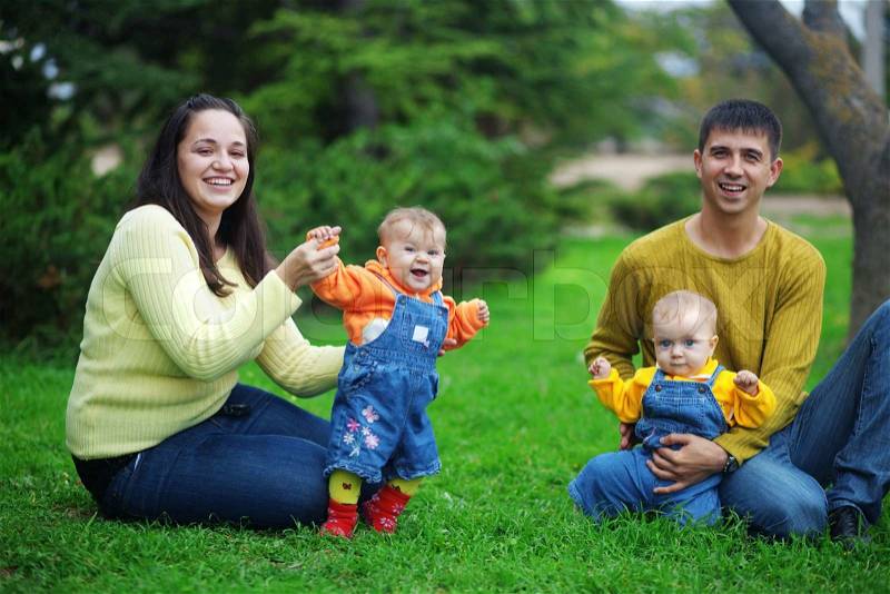Portrait of happy young parents with their two babies twins having fun in park, stock photo