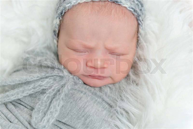 Sleeping frowning baby with gray knitted hat on, wrapped in gray blanket on pillow, topview, stock photo