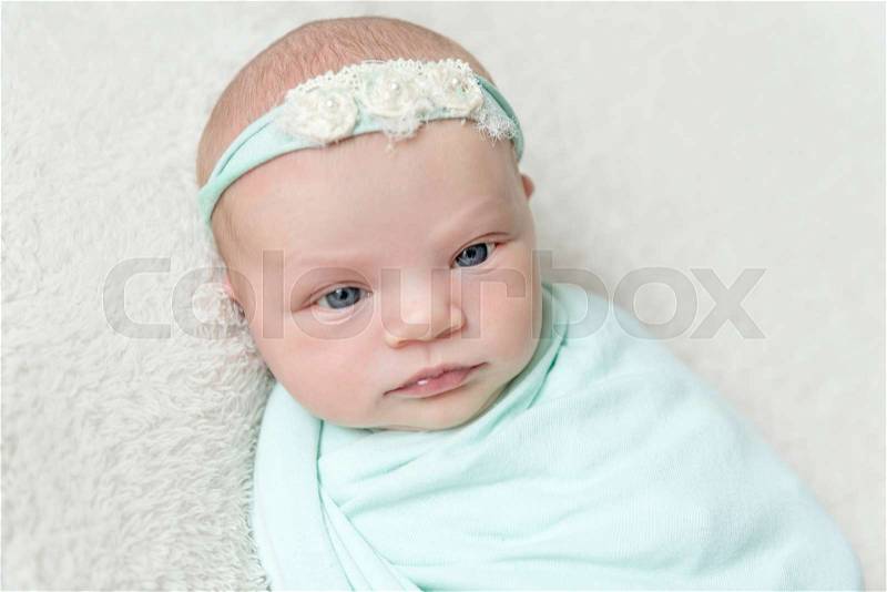 Lovely kid with eyes wide open wrapped up, blue hairband on her head, topview, stock photo