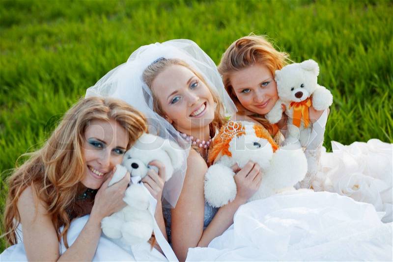 Three happy brides with teddy bears posing on fresh green grass, stock photo