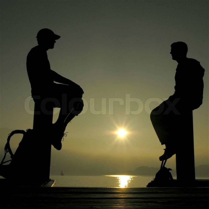 Silhouettes of two men against the sun, stock photo