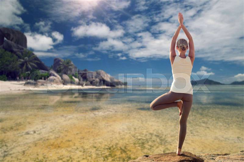Fitness, sport, people and recreation concept - young woman making yoga tree pose from back over exotic tropical beach background, stock photo