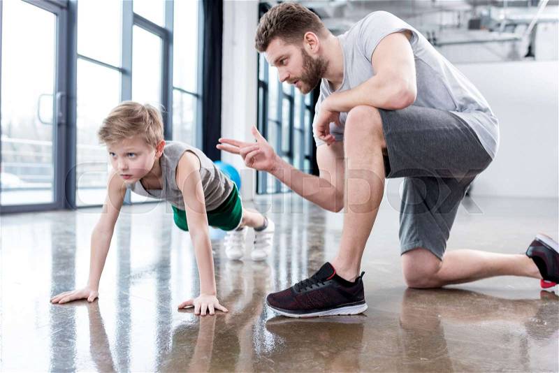 Boy doing push ups with coach at fitness center, stock photo
