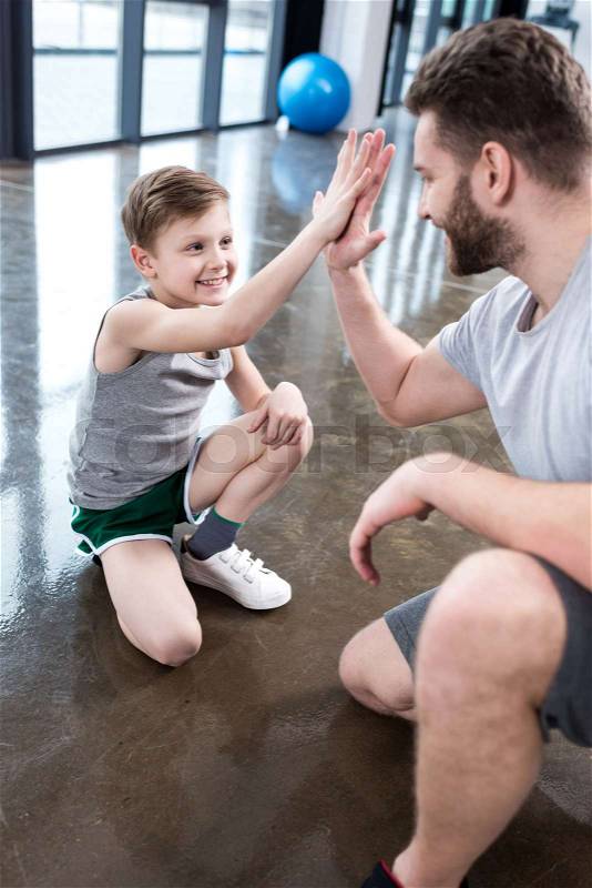 Boy giving high five to his adult friend at fitness center, stock photo