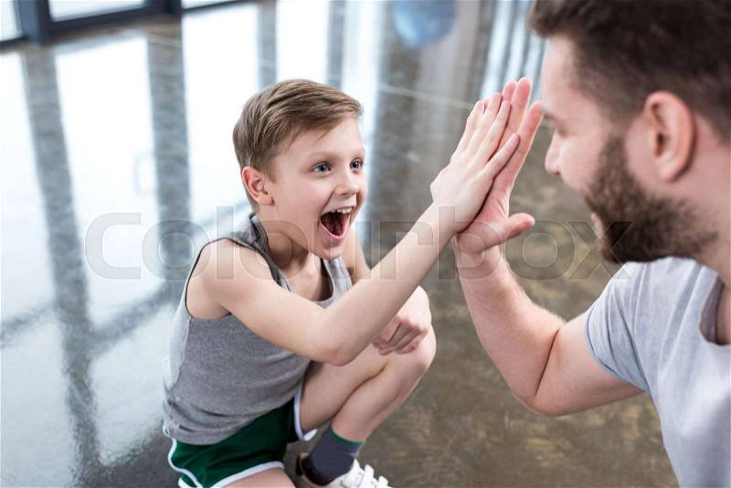 Boy giving high five to his adult friend at fitness center, stock photo