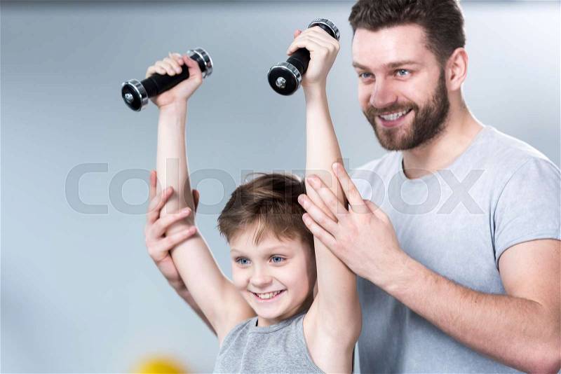 Boy training with dumbbells together with coach at fitness center, stock photo