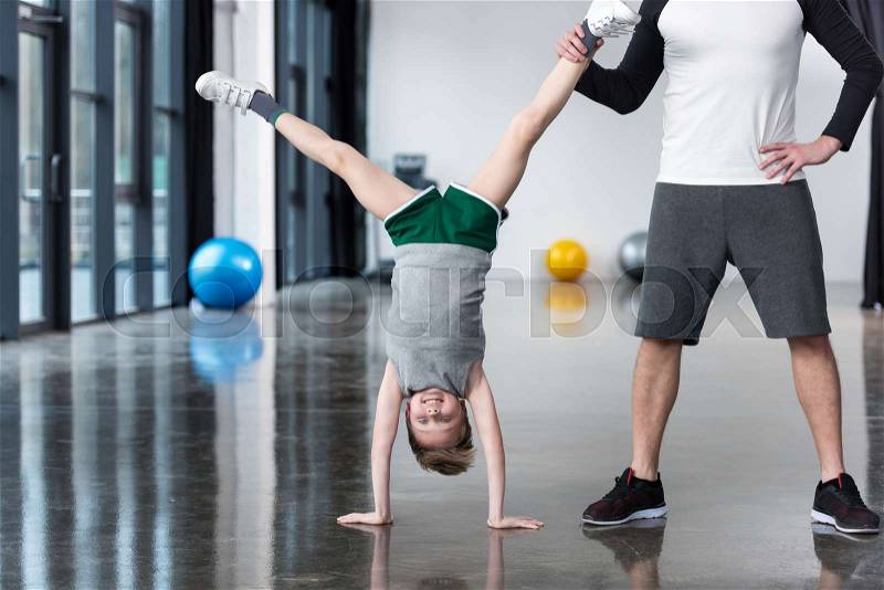 Trainer helping boy standing on hands at exercise room, stock photo