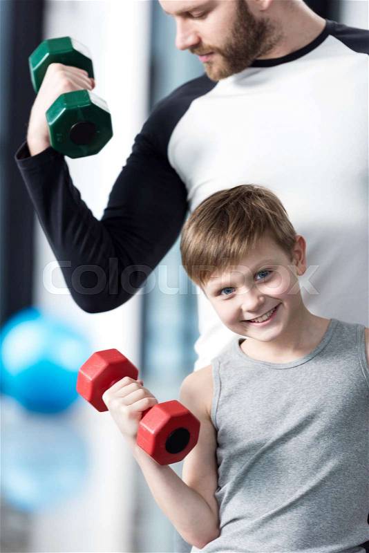 Boy training with dumbbells together with coach at fitness center, stock photo