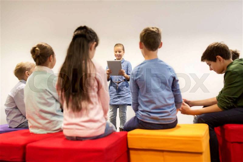 Education, children, learning, technology and people concept - happy girl with tablet pc computer presenting something to group of kids at school, stock photo