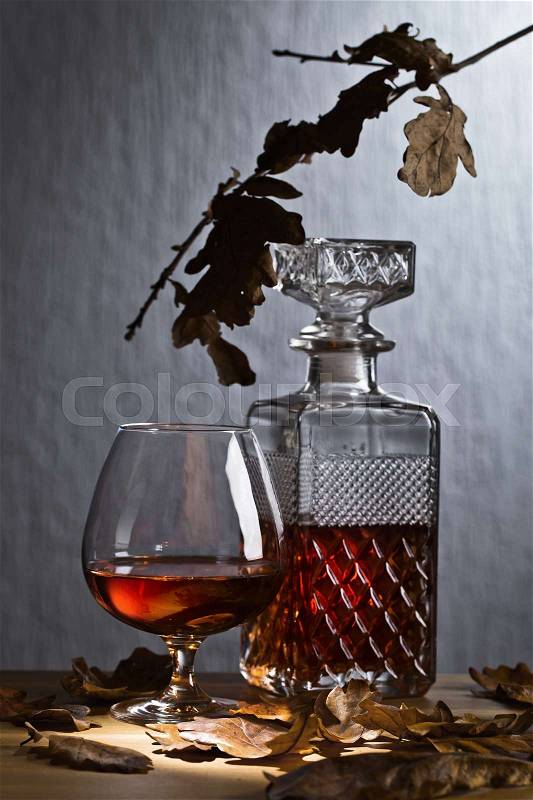 Snifter and decanter of brandy . Dried oak leaves on a wooden table . , stock photo