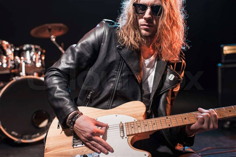 Handsome rock star in eyeglasses playing hard rock music with bass guitar on stage, stock photo