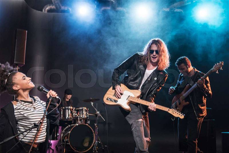 Singer with microphone and electric guitar players performing concert on stage , stock photo