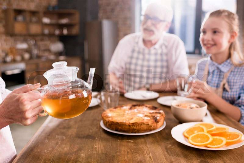 Grandparents and girl drinking tea with pie together at home, stock photo