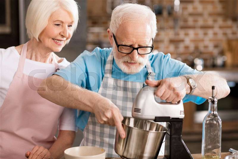 Happy senior husband and wife cooking together and mixing dough , stock photo