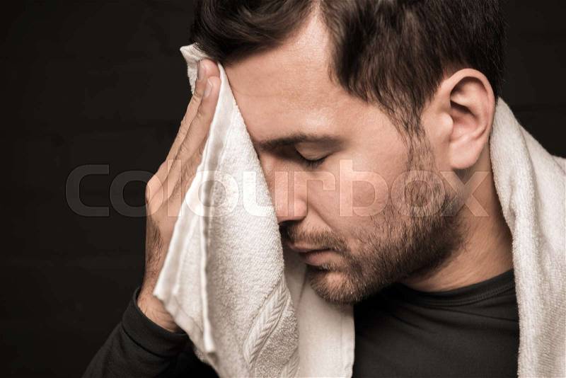 Tired sportsman wiping face by towel at gym locker room, stock photo
