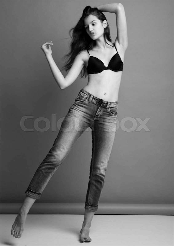 Model test portrait with young beautiful fashion model posing on grey background. Black bra and jeans, stock photo