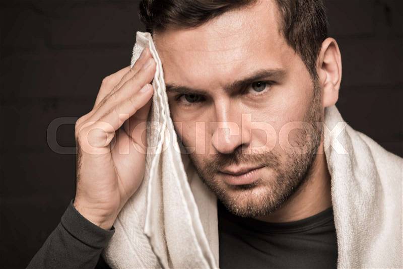 Tired sportsman wiping face by towel at gym locker room, stock photo