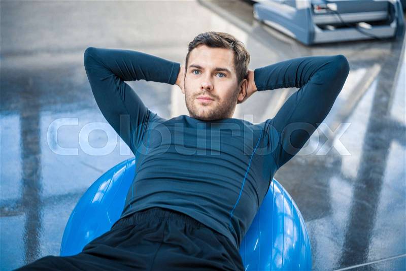 Handsome young man exercising on fitness ball at gym, stock photo