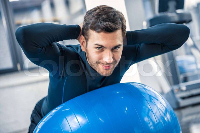 Handsome young man exercising on fitness ball at gym, stock photo