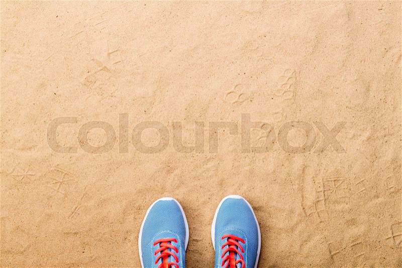 Blue sports shoes with pink shoelaces laid on sand beach background, studio shot, flat lay. Copy space, stock photo