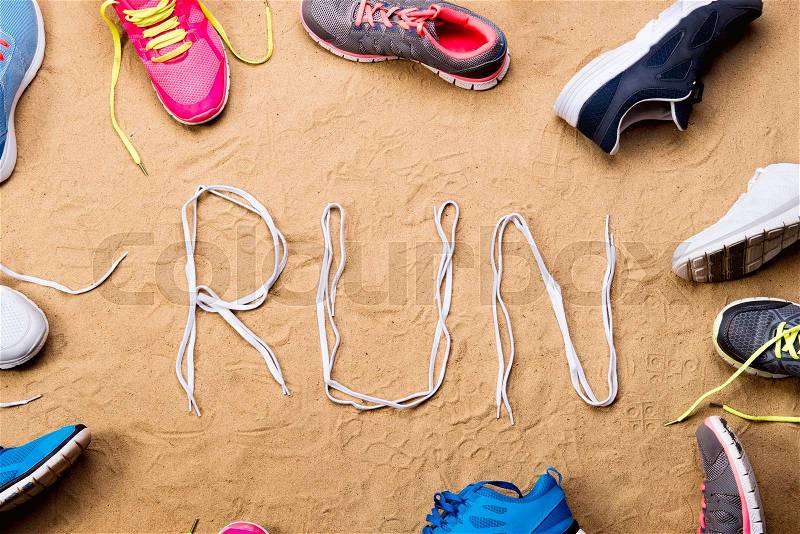 Various running shoes and run sign made of shoelaces against sand background, studio shot, flat lay, stock photo