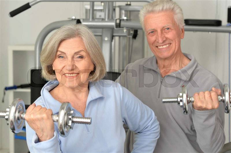 Beautiful elderly couple in a gym with dumbbells, stock photo