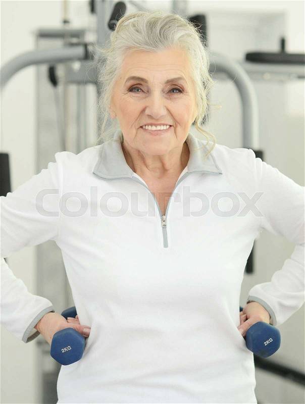 Portrait of a beautiful elderly woman in a gym with dumbbells, stock photo