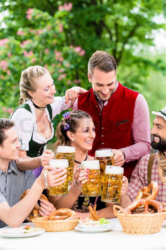 In Beer garden - friends in Tracht, Dirndl and Lederhosen drinking a fresh beer in Bavaria, Munich, Germany, stock photo