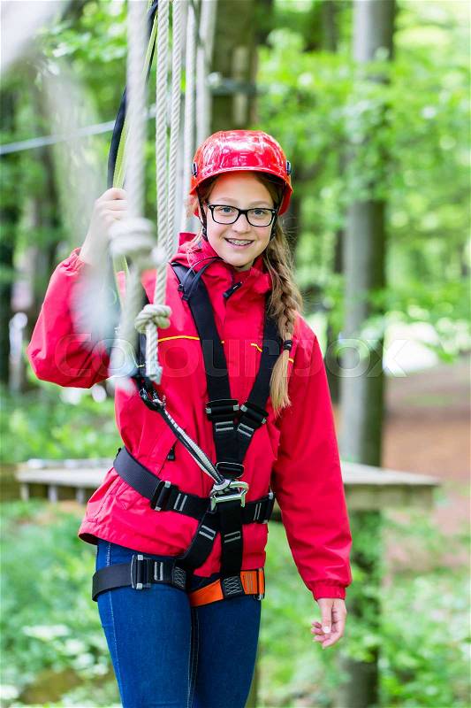 Girl roping up in high rope course exercising the necessary safety precautions, stock photo