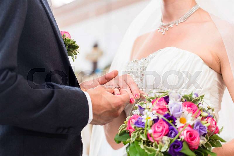 Groom slipping ring on finger of bride at wedding, stock photo
