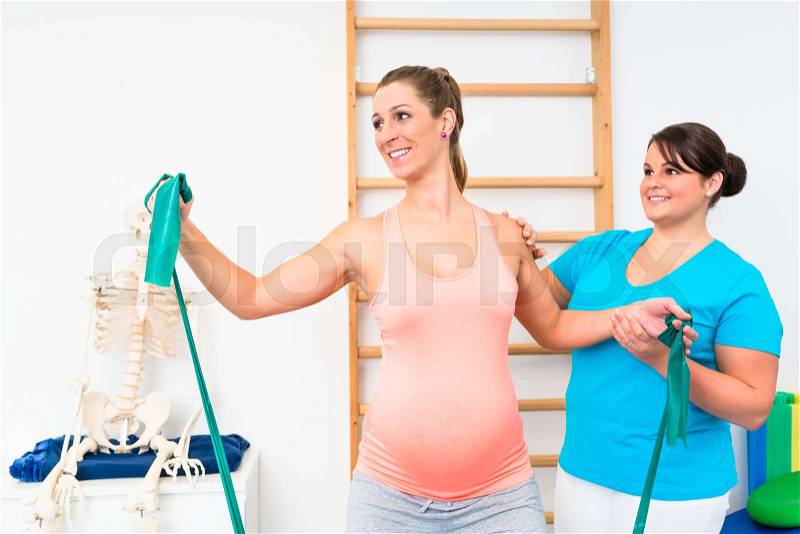 Pregnant woman exercising with resistance band in physiotherapy, stock photo
