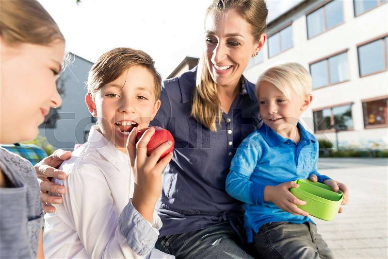 Mother and kids at school having breaktime with apple and lunchbox , stock photo