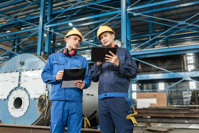 Two Asian experts checking information during quality control in the interior of a factory, stock photo