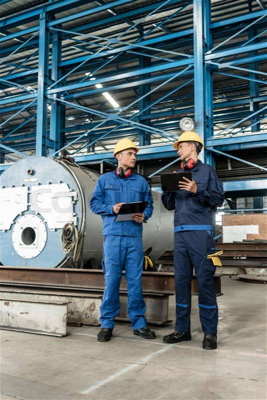 Two Asian experts checking information during quality control in the interior of a factory, stock photo