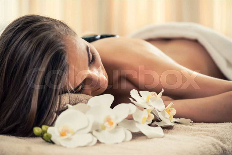 High angle view of young woman lying down on massage bed with traditional hot stones along the spine at spa and wellness center , stock photo