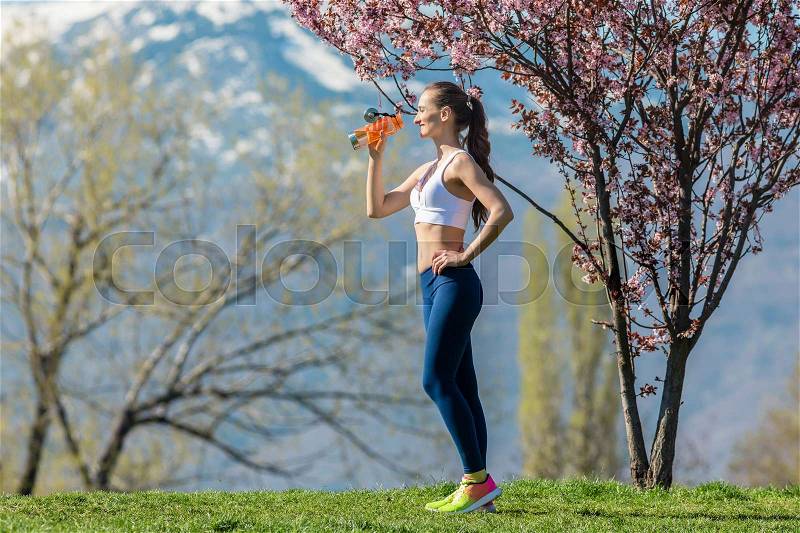 Woman having break from running drinking water, stock photo
