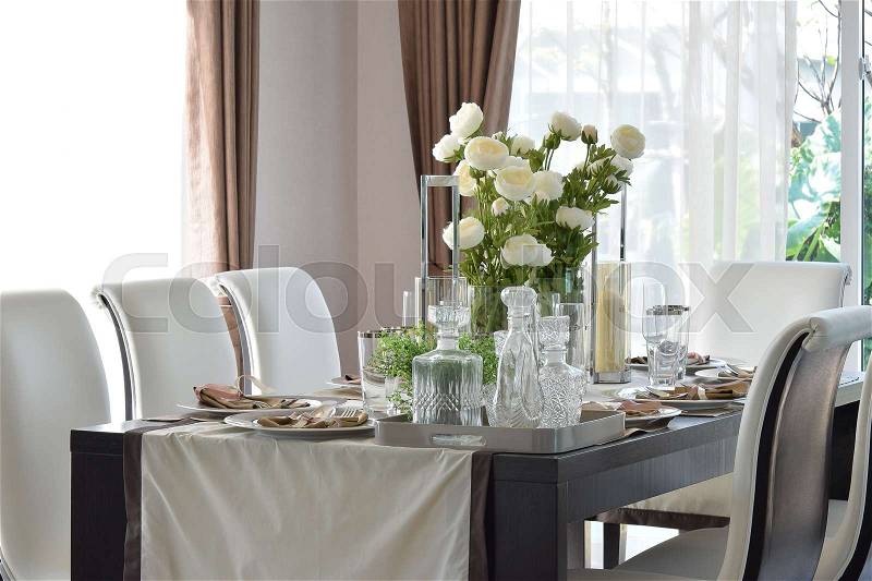 Dining wooden table and comfortable chairs in modern home with elegant table setting, stock photo
