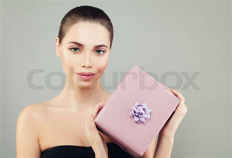 Smiling Model Woman with Perfect Skin and Makeup Holding Gift Box on Banner Background, stock photo